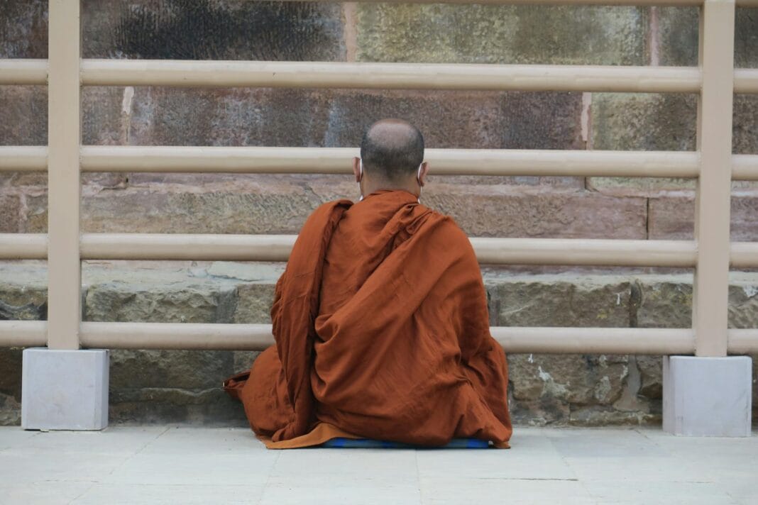 Mnich w pomarańczowych szatach medytuje przy kamiennej ścianie