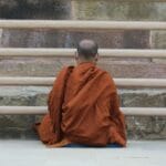 Mnich w pomarańczowych szatach medytuje przy kamiennej ścianie
