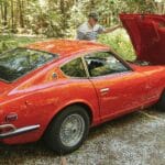 Starszy mężczyzna sprawdza silnik klasycznego czerwonego Datsuna 240Z