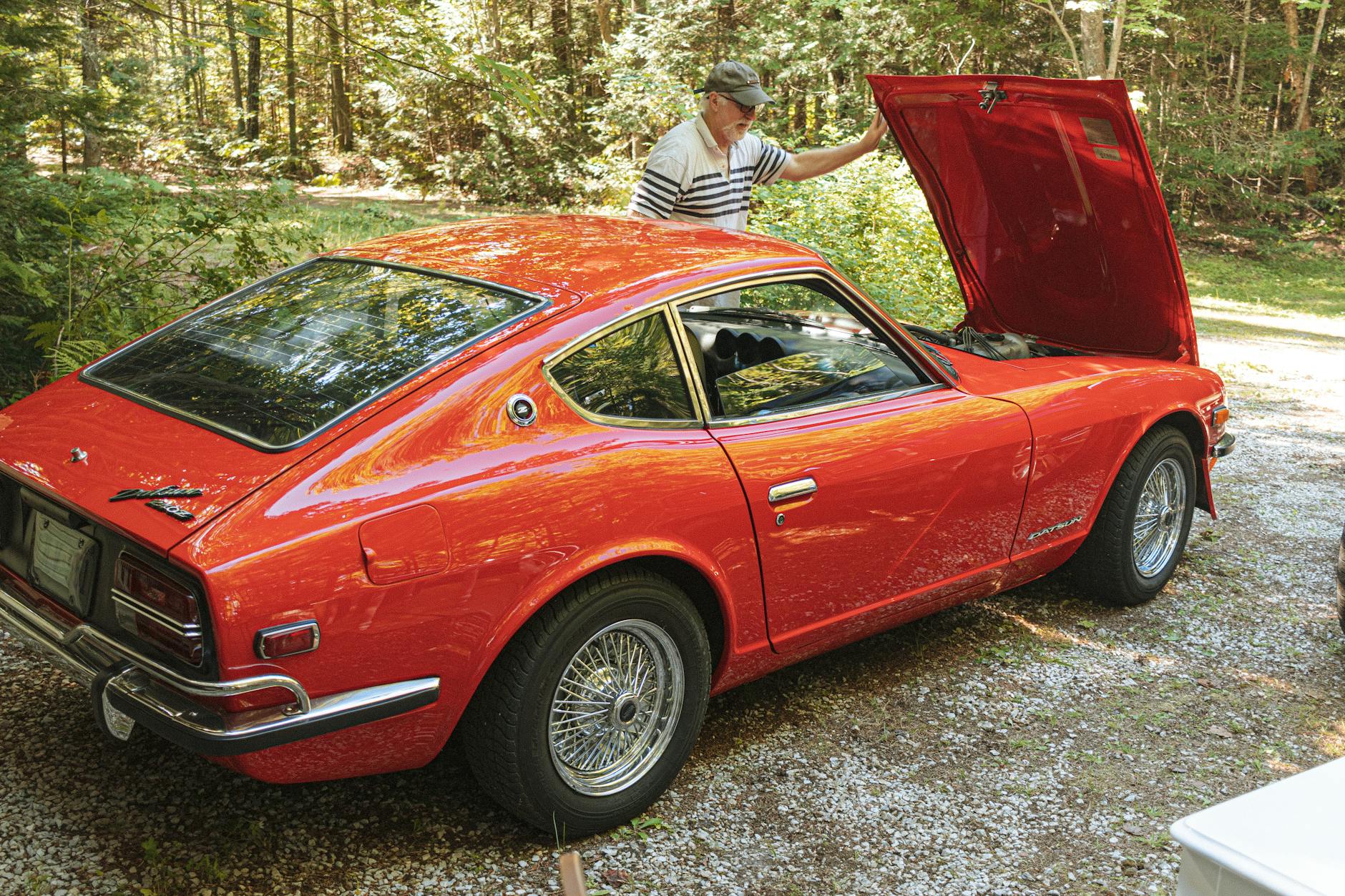 Starszy mężczyzna sprawdza silnik klasycznego czerwonego Datsuna 240Z