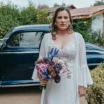 Panna młoda z bukietem pozuje przy zabytkowym aucie w ogrodzie