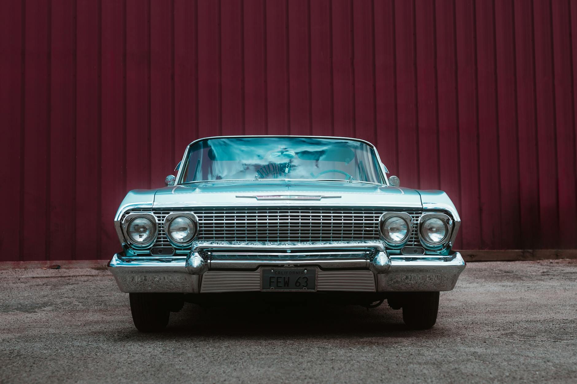 Przód klasycznego auta z PRL zaparkowanego przy czerwonej ścianie