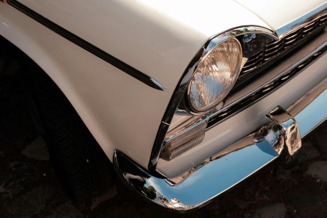 Zbliżenie na chromowany grill i reflektor zabytkowego auta z PRL