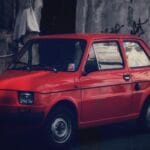 Czerwony Fiat 126p zaparkowany przy ulicy w miejskiej zabudowie