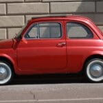 Czerwony klasyczny Fiat 500 zaparkowany przy ceglanej ścianie w mieście